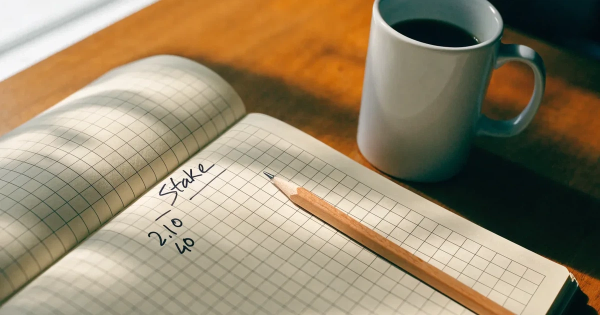 Ein Taschenrechner und ein Bleistift liegen auf kariertem Papier neben einer Tasse Kaffee, ein Fensterplatz mit Tageslicht.