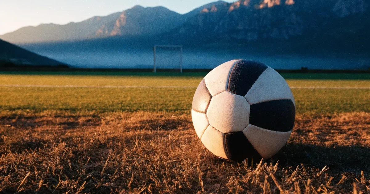 Ein Fussball auf einem staubigen Rasenstück in der Abendsonne, im Hintergrund eine hohe Bergkette