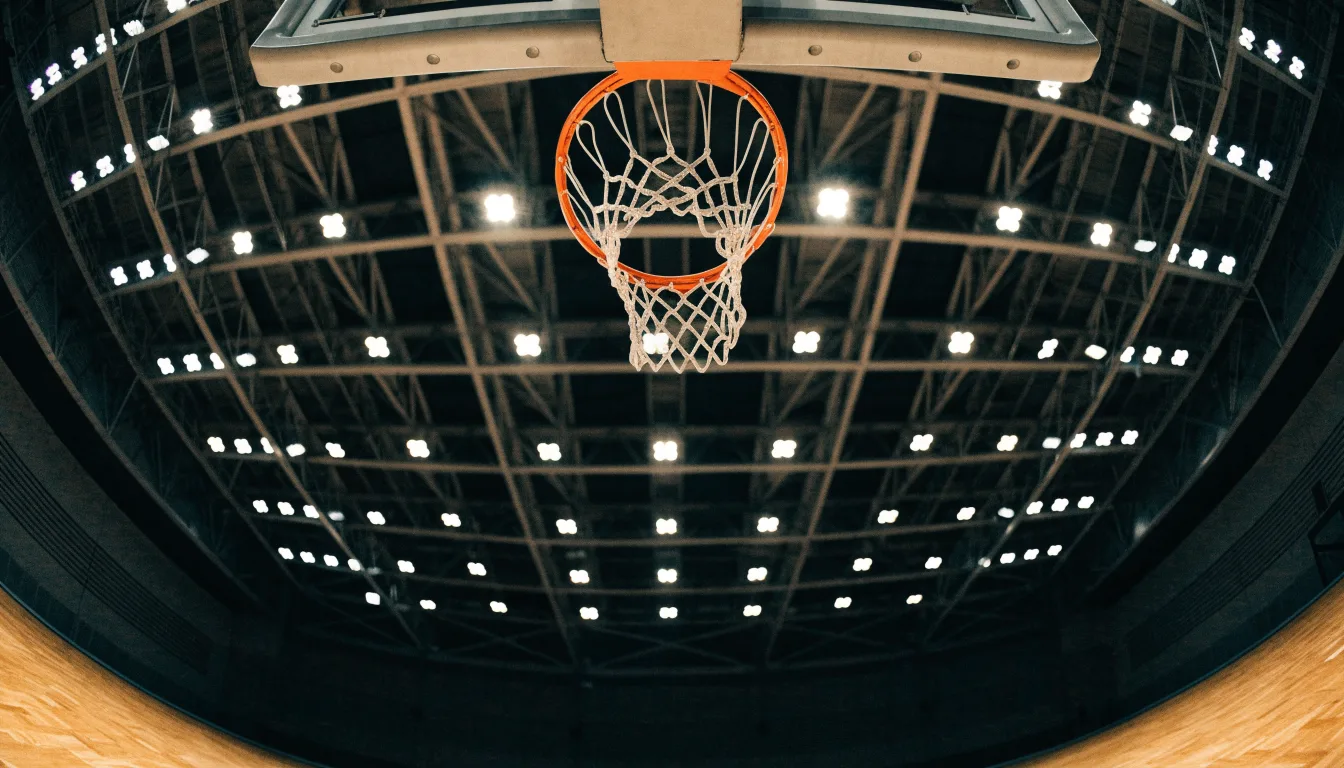 Ein Basketballkorb von unten gesehen, darüber eine Hallendecke mit Scheinwerfern und Stahlträgern.