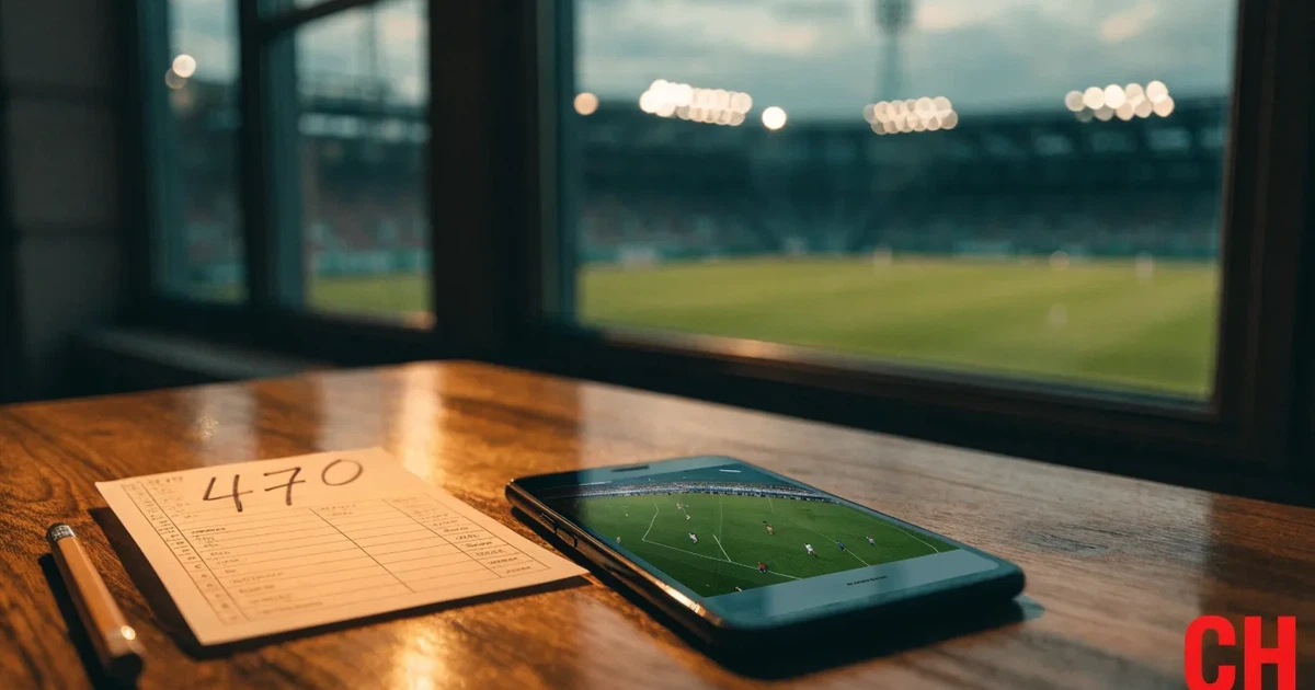 Ein Fussball liegt auf dem Anstosspunkt eines leeren Rasenplatzes in der Abenddämmerung, dahinter leuchten Flutlichtmasten über einer Tribüne.